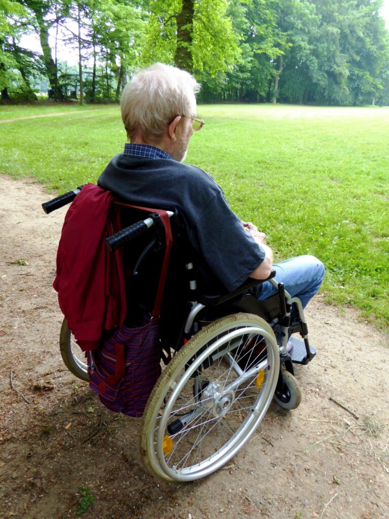 Un hombre anciano con templando la naturaleza sentado en una silla de ruedas.