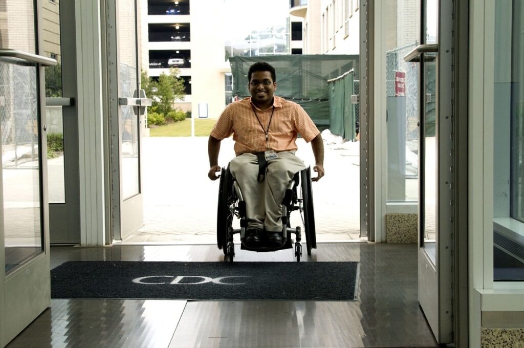 Un hombre entrando a un edificio sobre su silla de ruedas y sonriendo felizmente.